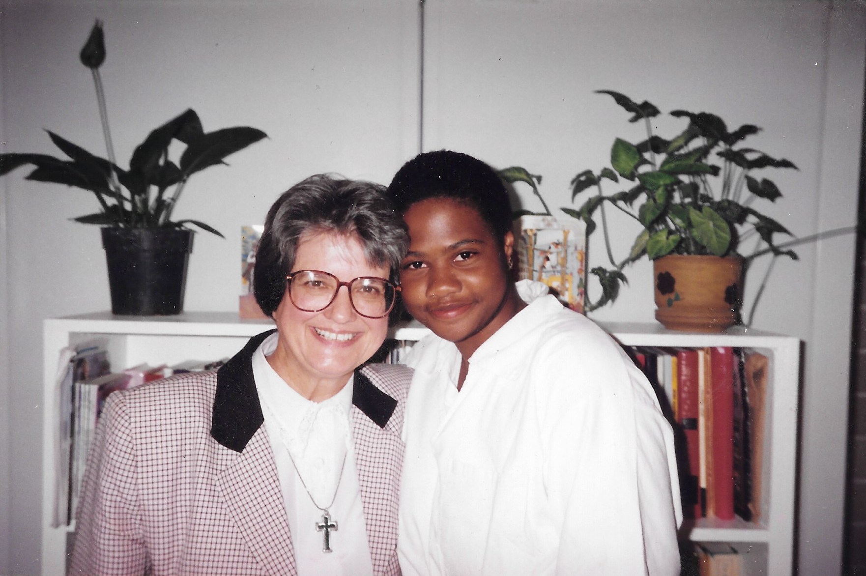 Two women with their arms around each other, in front of a bookcase.